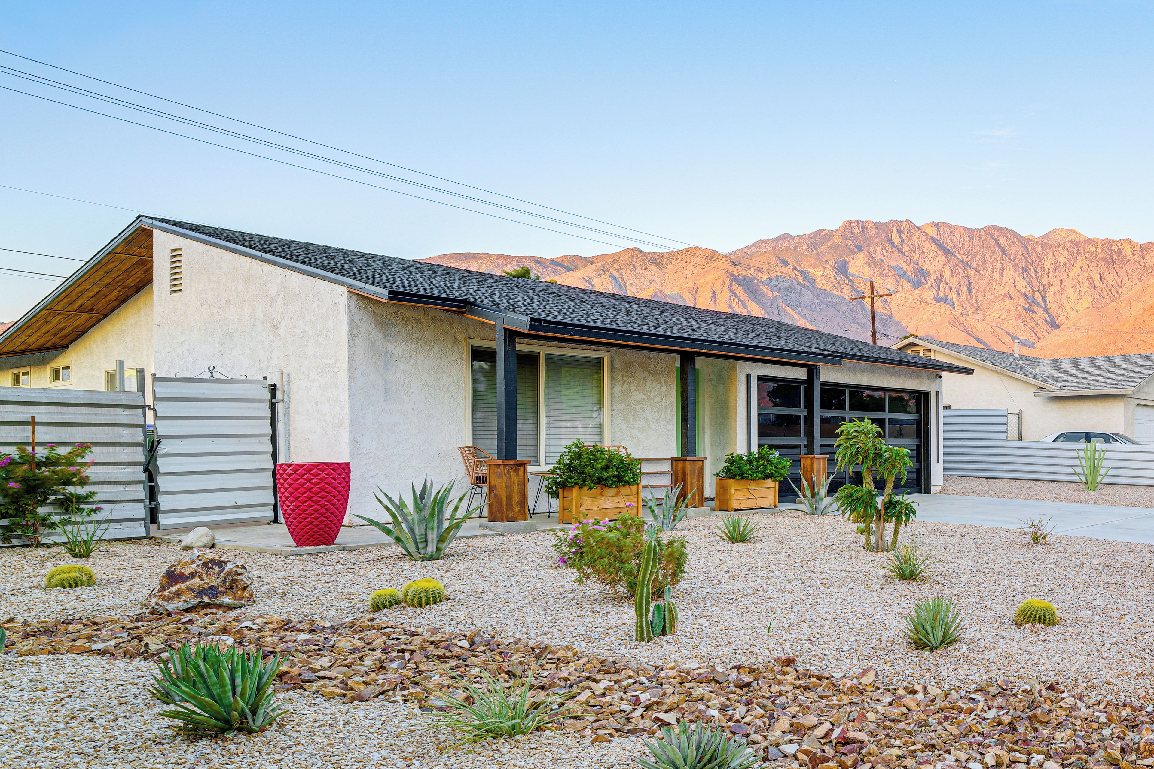 Una casa moderna con techo inclinado, un garaje y un jardín con cactus y suculentas.