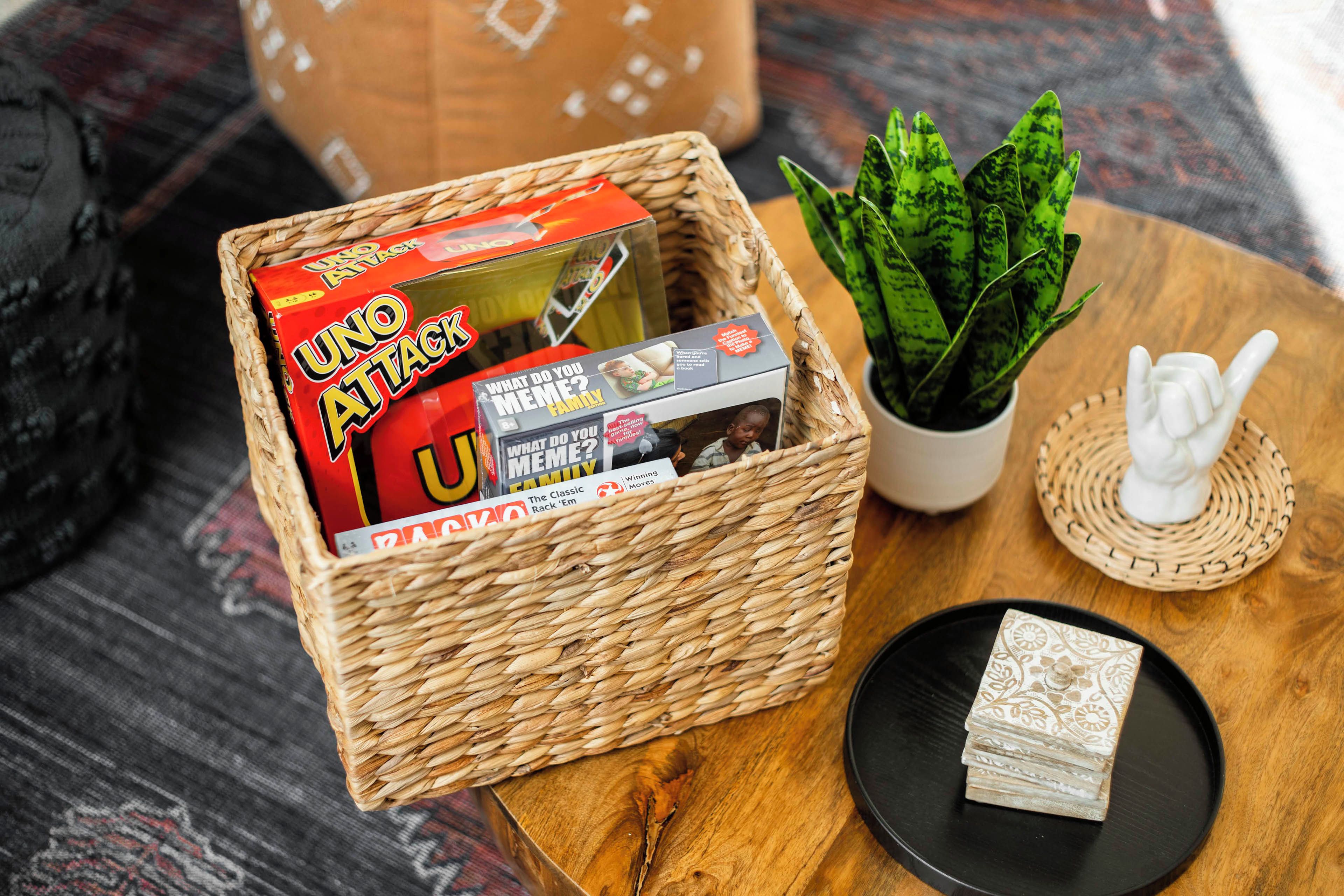 A woven basket containing board games, a potted plant, and a small statue on a wooden table.