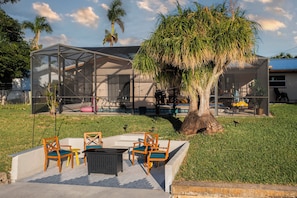 A modern outdoor seating area with a glass enclosure, a tree, and a pool. - Pool & Dock! Walk to Downtown Dining & Nightlife (Cape Coral)