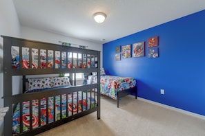 Een kamer met stapelbedden en een blauwe muur, met beddengoed en kunst aan de muur in superhelden thema.