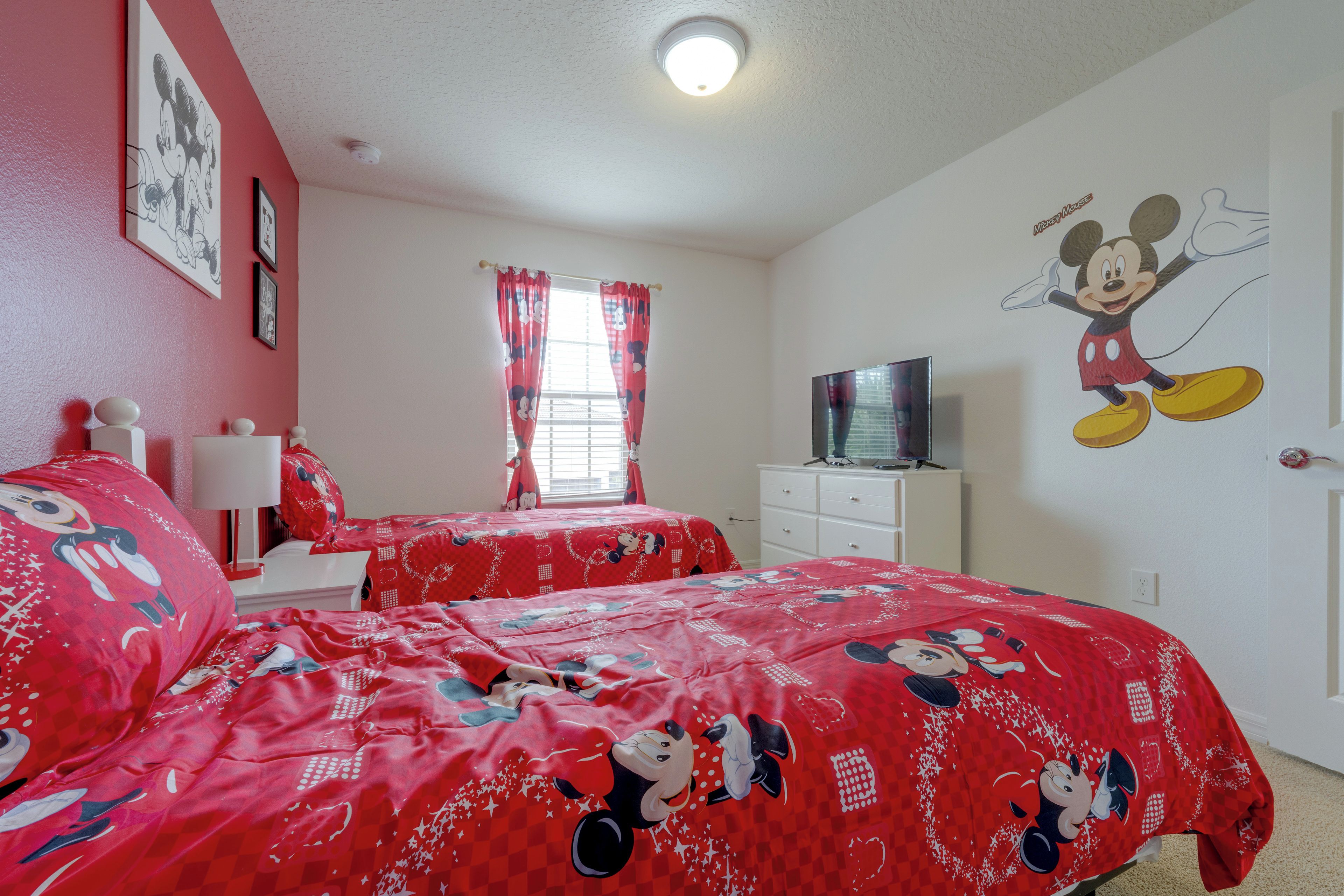 A room with two beds, a television on a dresser, and Mickey Mouse wall art.