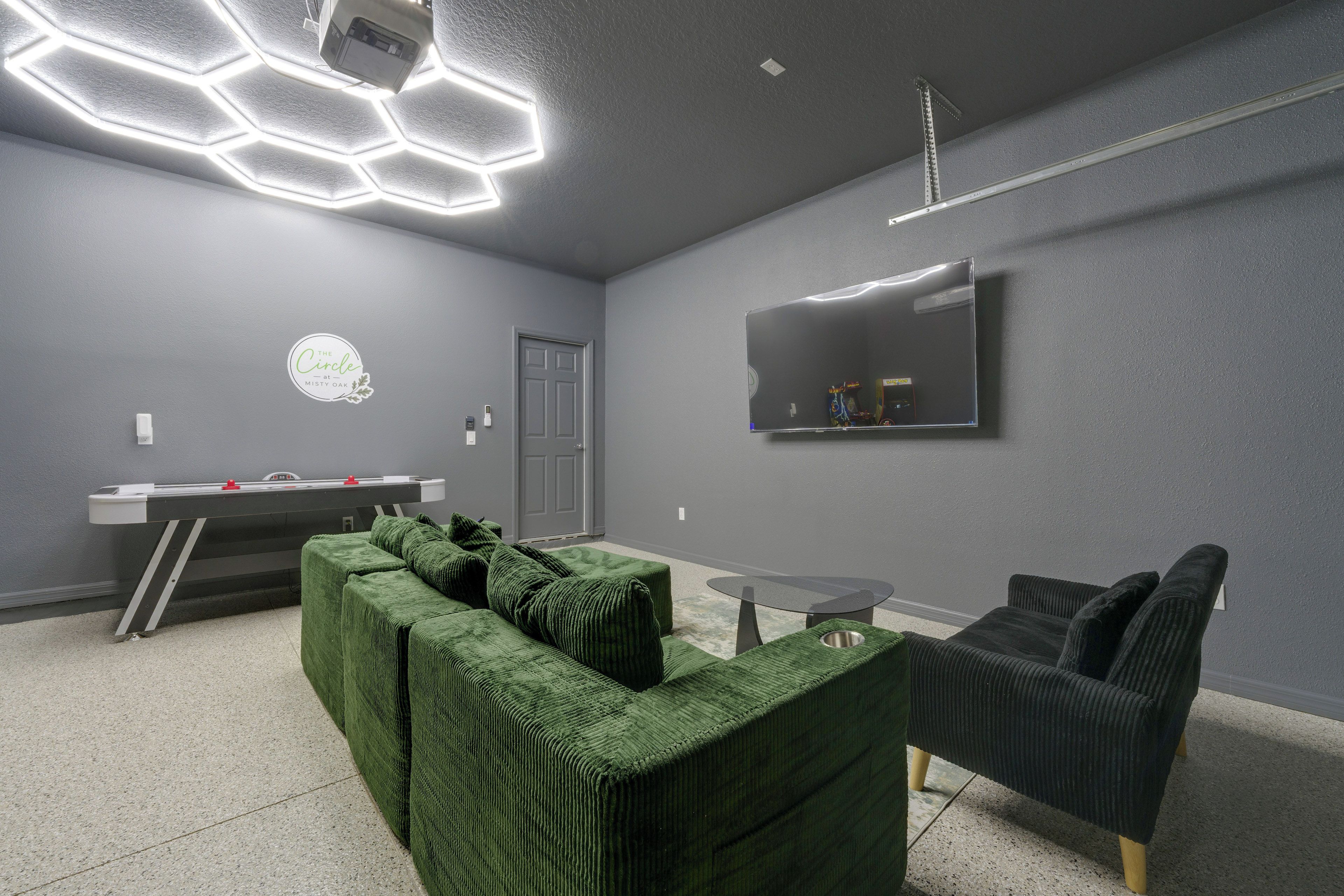 A modern room with a green sectional sofa, a small round table, a flat-screen TV mounted on the wall, and a grey door.