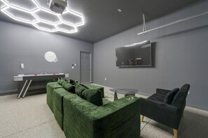 A modern room with a green sectional sofa, a small round table, a flat-screen TV mounted on the wall, and a grey door. - Solterra Resort Home w/ AI Vending & Private Pool! (Davenport)