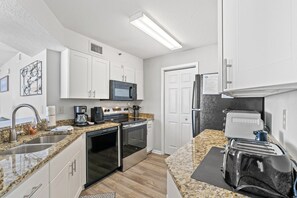 A modern kitchen with white cabinets, a microwave, a stove, a refrigerator, and a toaster. - 3-bedroom, 2-bathroom, oceanfront condo, Plenty of updates and upgrades | Sea Castle - 3D (North Myrtle Beach)