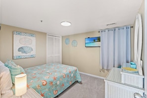 A bedroom with a bed, a nightstand, a lamp, a television, and a bathroom with a shower curtain. - 3-bedroom, 2-bathroom, oceanfront condo, Plenty of updates and upgrades | Sea Castle - 3D (North Myrtle Beach)