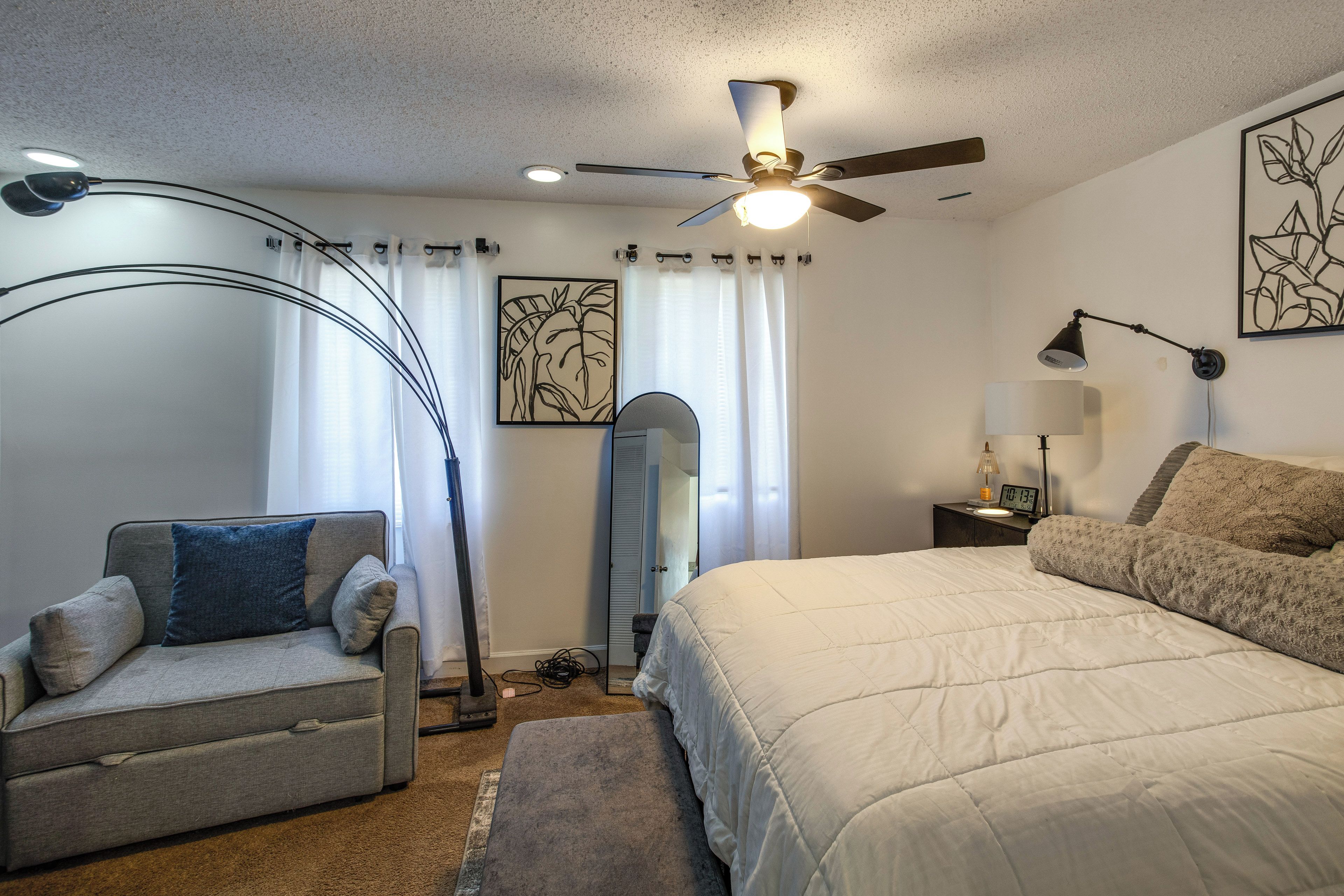 A bedroom with a bed, a chair, a desk, a ceiling fan, and artwork on the walls.