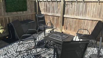 A patio with a grill, chairs, and a patterned rug.