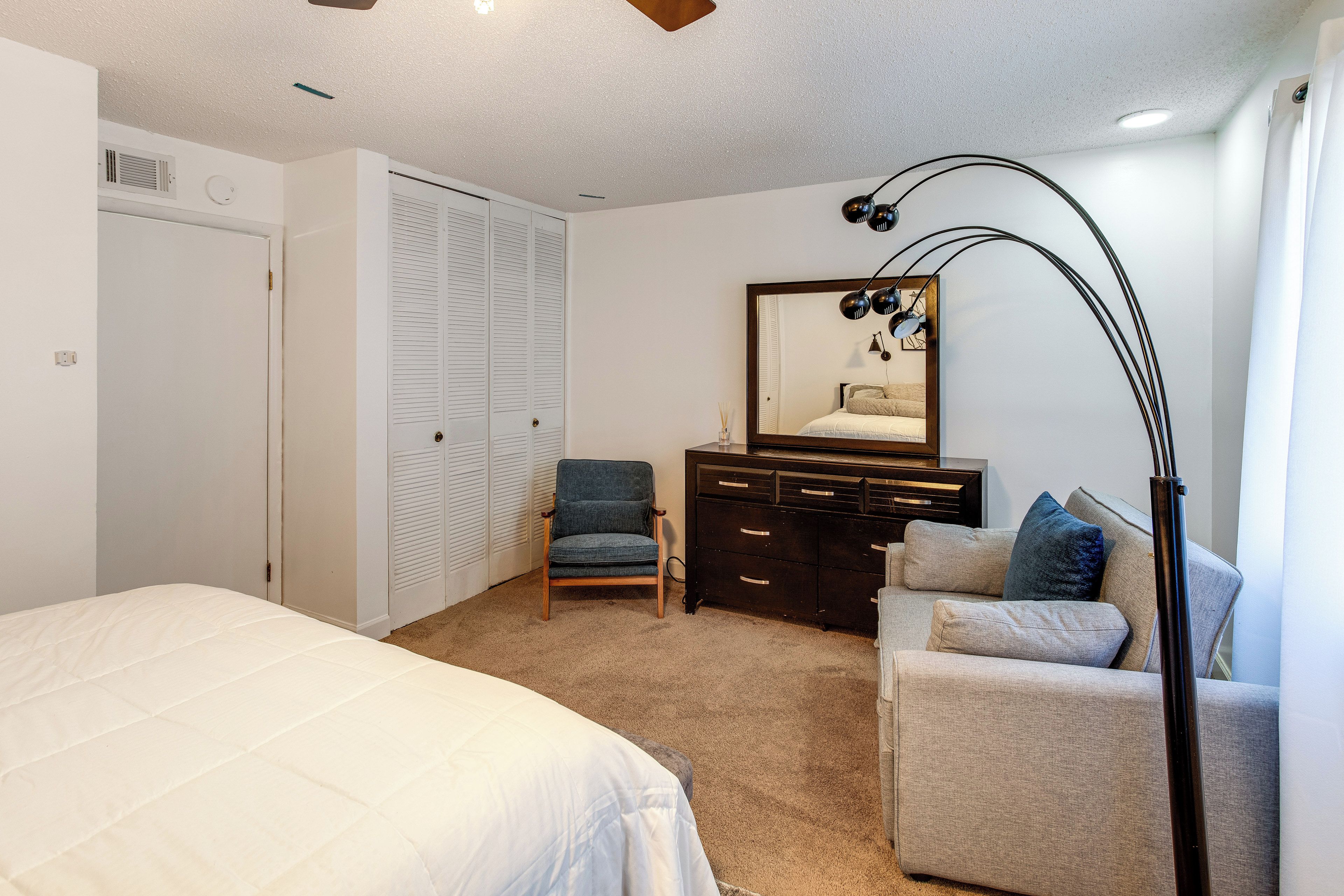 Quarto com cama, cadeira, cômoda, espelho e luminária.