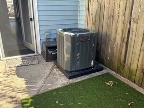 An outdoor air conditioning unit next to a house with a wooden fence and a door.