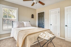 A bedroom with a bed, a ceiling fan, a window, and a door.