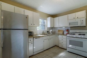 A kitchen with white cabinets, a stainless steel refrigerator, a microwave, a stove, and a toaster.