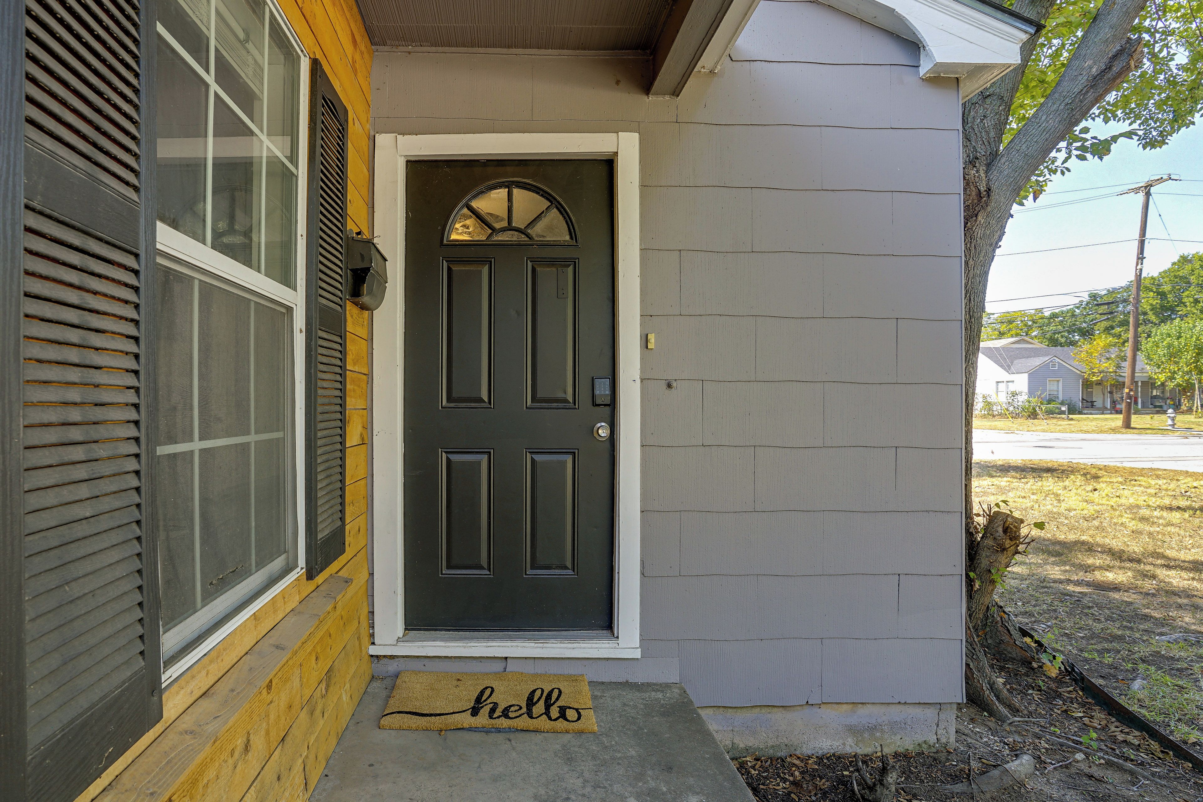 A house with a dark front door, a yellow doormat with 'hello' written on it, and a window with blinds.