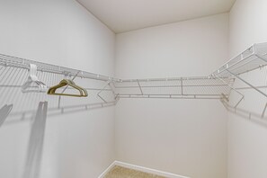 A corner of a room with a white ceiling and walls, a metal wire shelf with clothes, and a small section of a beige carpet. - Screened Porch: Newly Built Townhome in Madison (Madison)