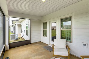 A covered porch with a sliding glass door, a wooden floor, and a white cushioned chair. - Screened Porch: Newly Built Townhome in Madison (Madison)