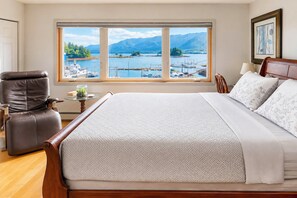 A bedroom with a large bed, a chair, a small table with a glass container, and a view of a marina and mountains through a large window. - Ketchikan Oceanfront Retreat Dock On-site, Beach (Ketchikan)
