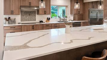 A modern kitchen with wooden cabinets, a marble island, and stainless steel appliances.