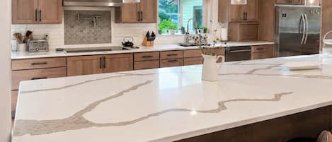 A modern kitchen with wooden cabinets, a marble island, and stainless steel appliances.