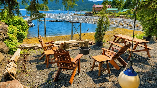 An outdoor seating area with wooden chairs and tables, a fire pit, and a view of a lake and dock.