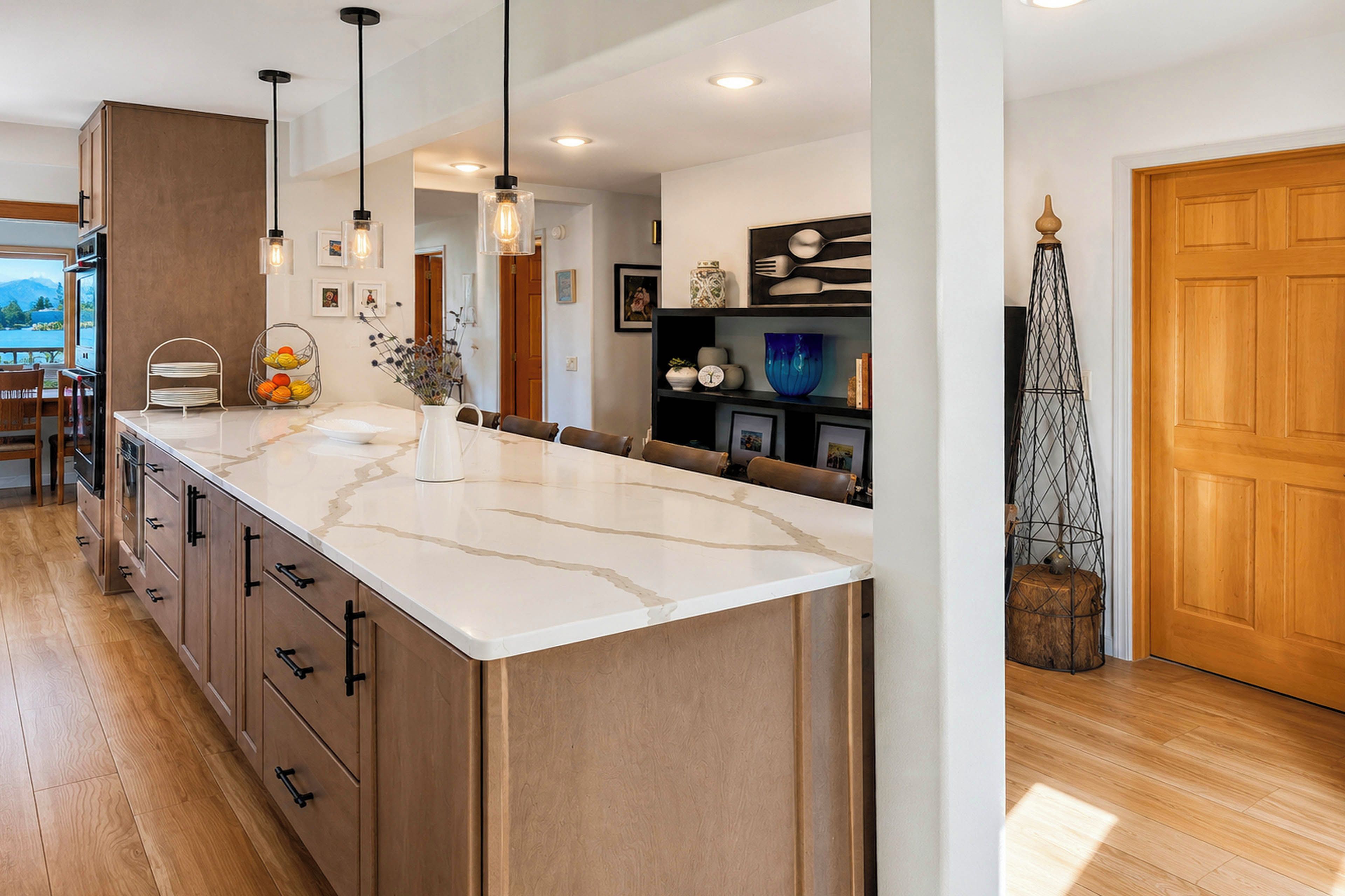 A modern kitchen with a large island, wooden cabinetry, pendant lighting, and a view of the outdoors.