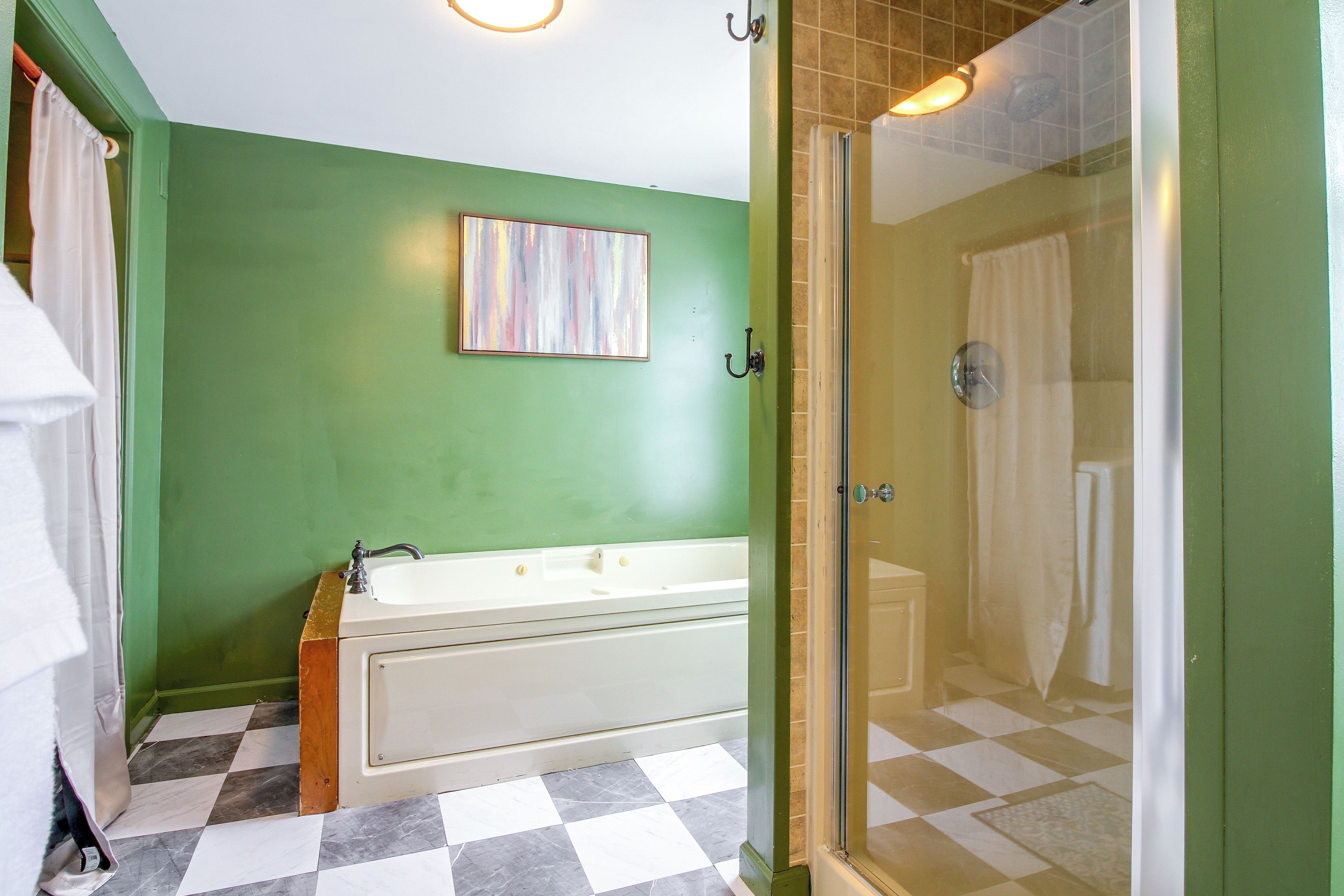 A bathroom with a white bathtub, a glass-enclosed shower, and a green wall.