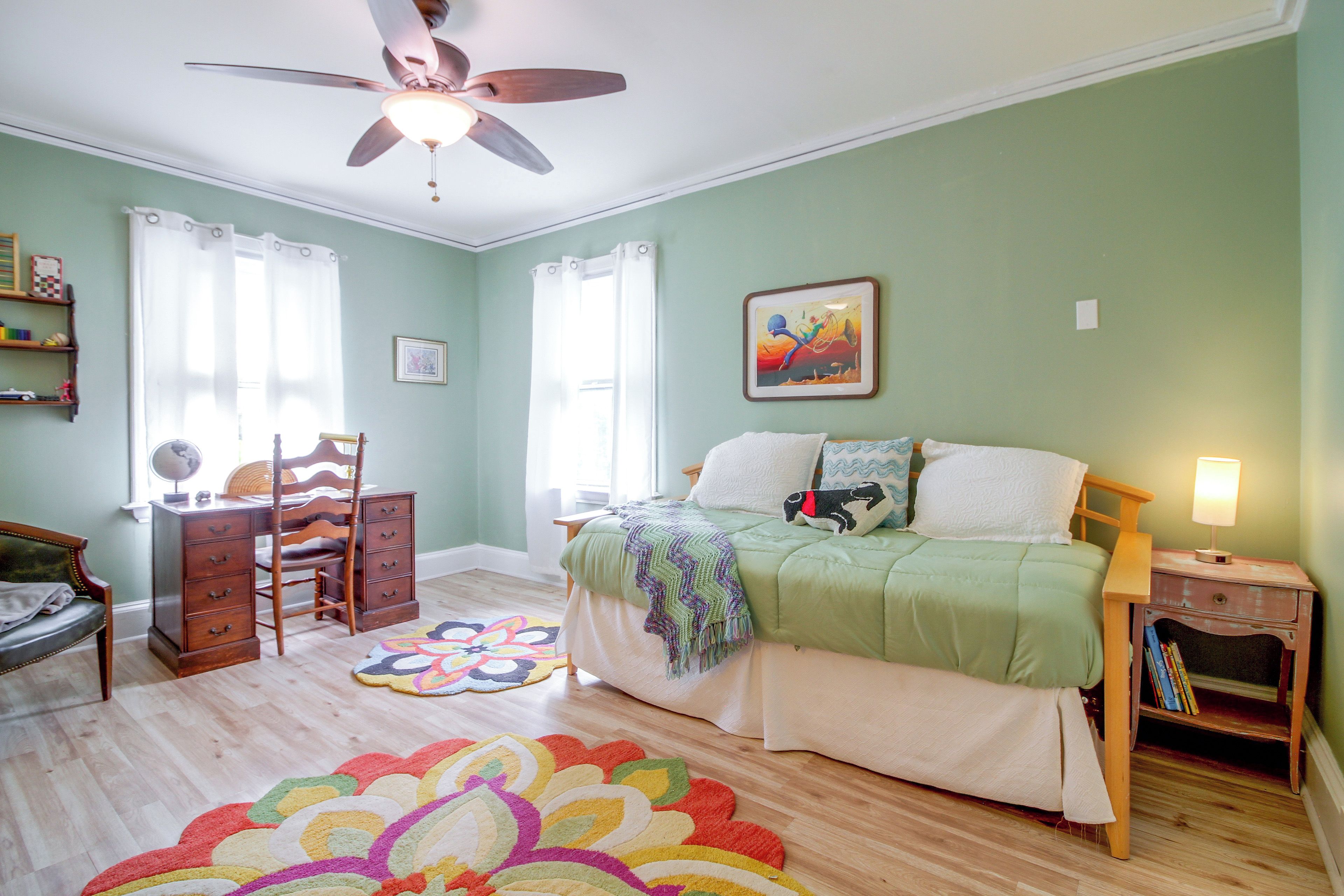 A bedroom with a bed, a nightstand, a chair, a dresser, a ceiling fan, and a colorful rug.