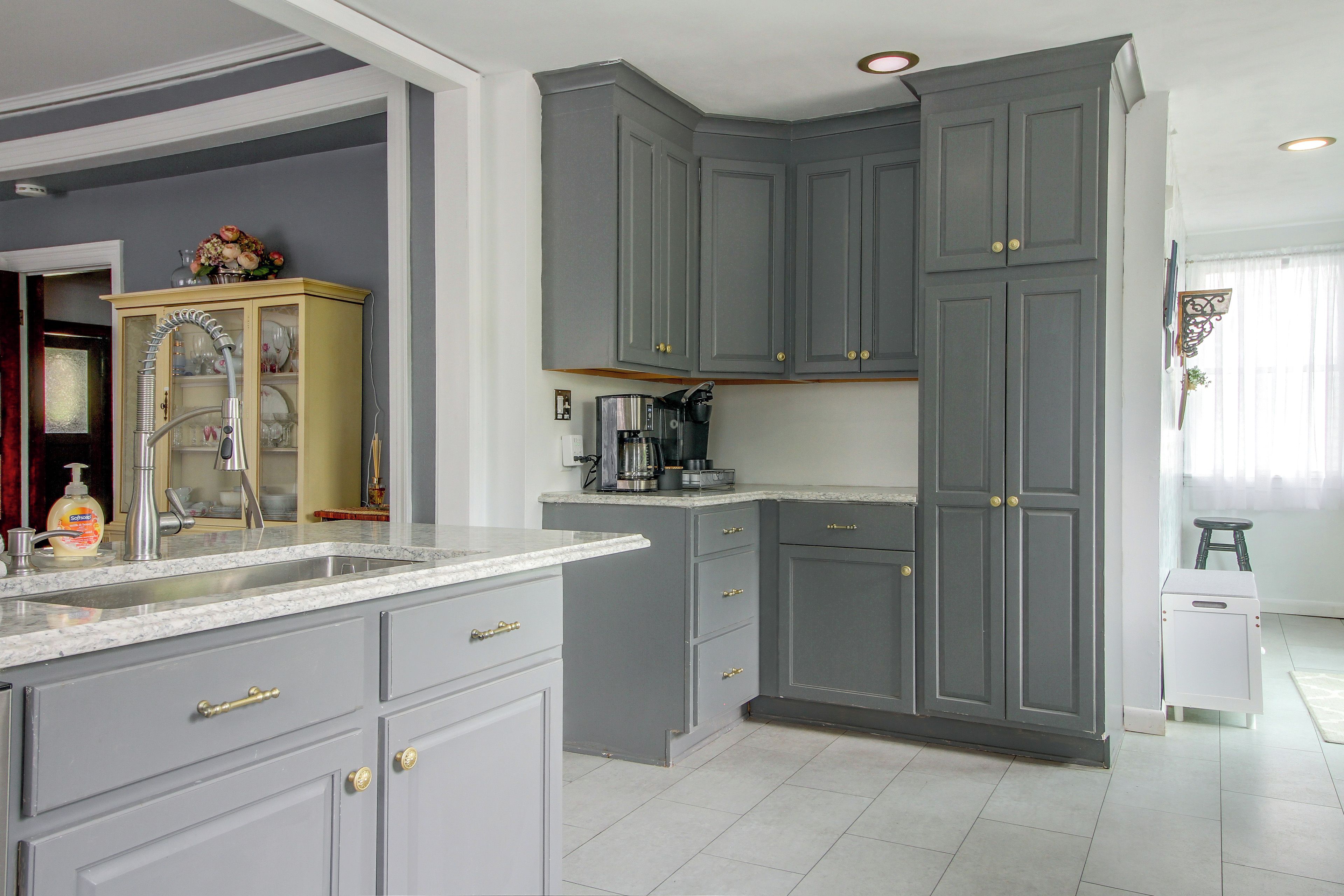 A kitchen with grey cabinets, a marble countertop, and a coffee machine.