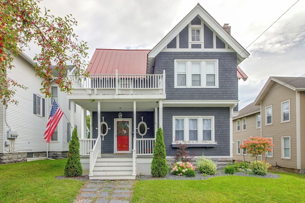 A two-story house with a front porch, a red door, and a flag.