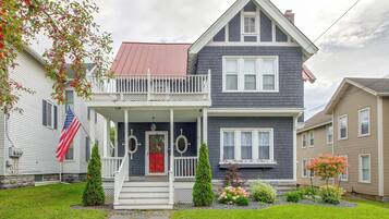 A two-story house with a front porch, a red door, and a flag.