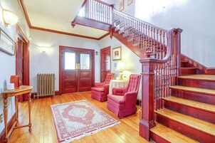 Una habitación amplia con una escalera de madera, un radiador, una mesa con lámpara y dos sillones.
