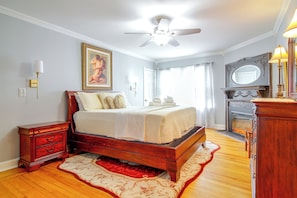 A bedroom with a wooden bed, a nightstand, a dresser, a fireplace, and a ceiling fan.