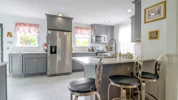 Una cocina moderna con armarios grises, electrodomésticos de acero inoxidable y una isla central con taburetes de bar.