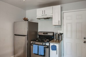 Una cocina compacta con nevera de acero inoxidable, cocina a gas y alacenas blancas.
