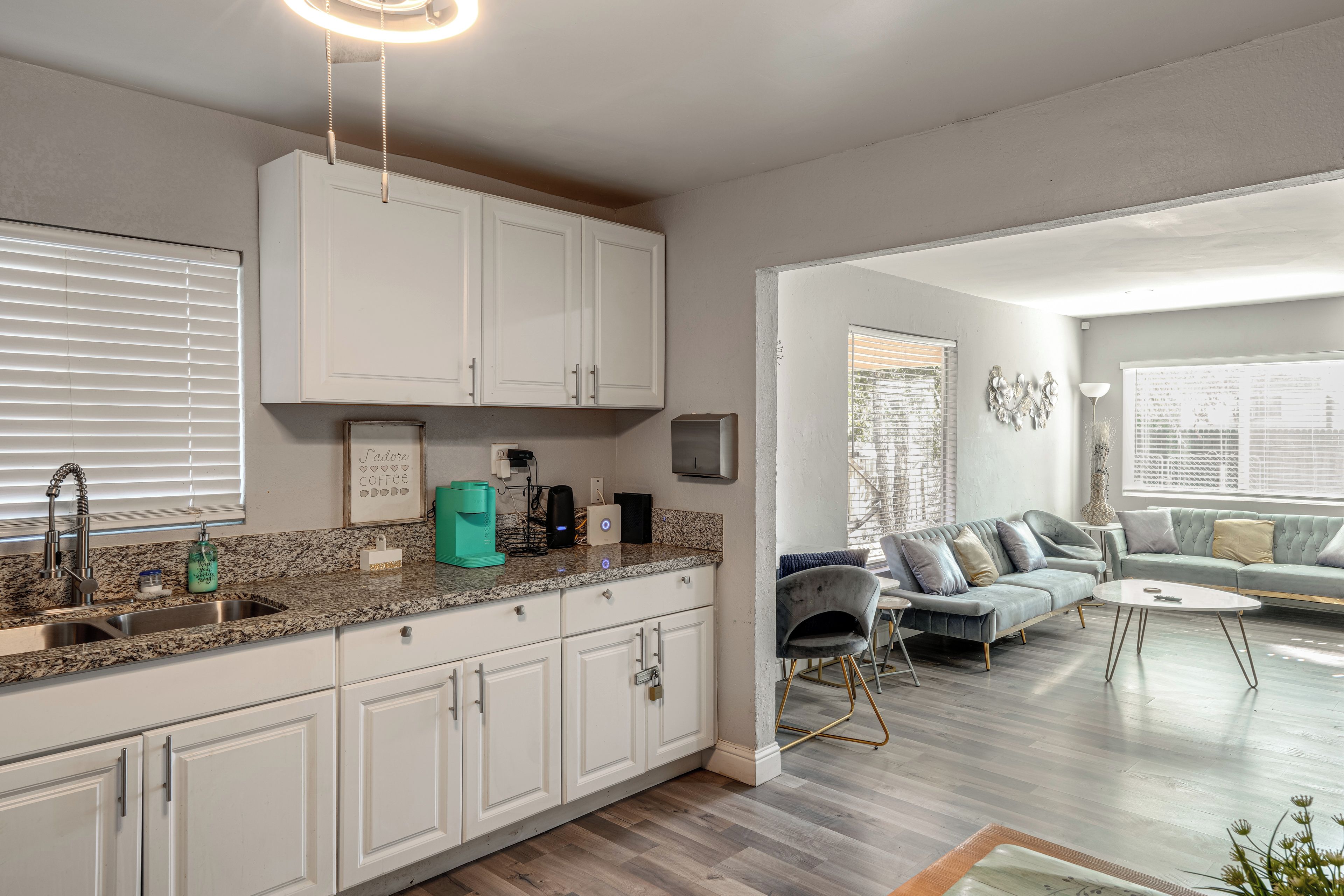 A modern kitchen with white cabinets, a granite countertop, and a coffee machine.