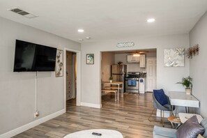 A modern living room with a flat-screen TV, a dining area with a table and chairs, and a kitchen with stainless steel appliances.