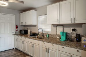 A kitchen with white cabinets, a granite countertop, a coffee maker, and a fire extinguisher.