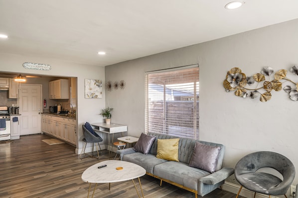 A modern living space with a kitchen, a dining area, and a seating area with a sofa and a round table.