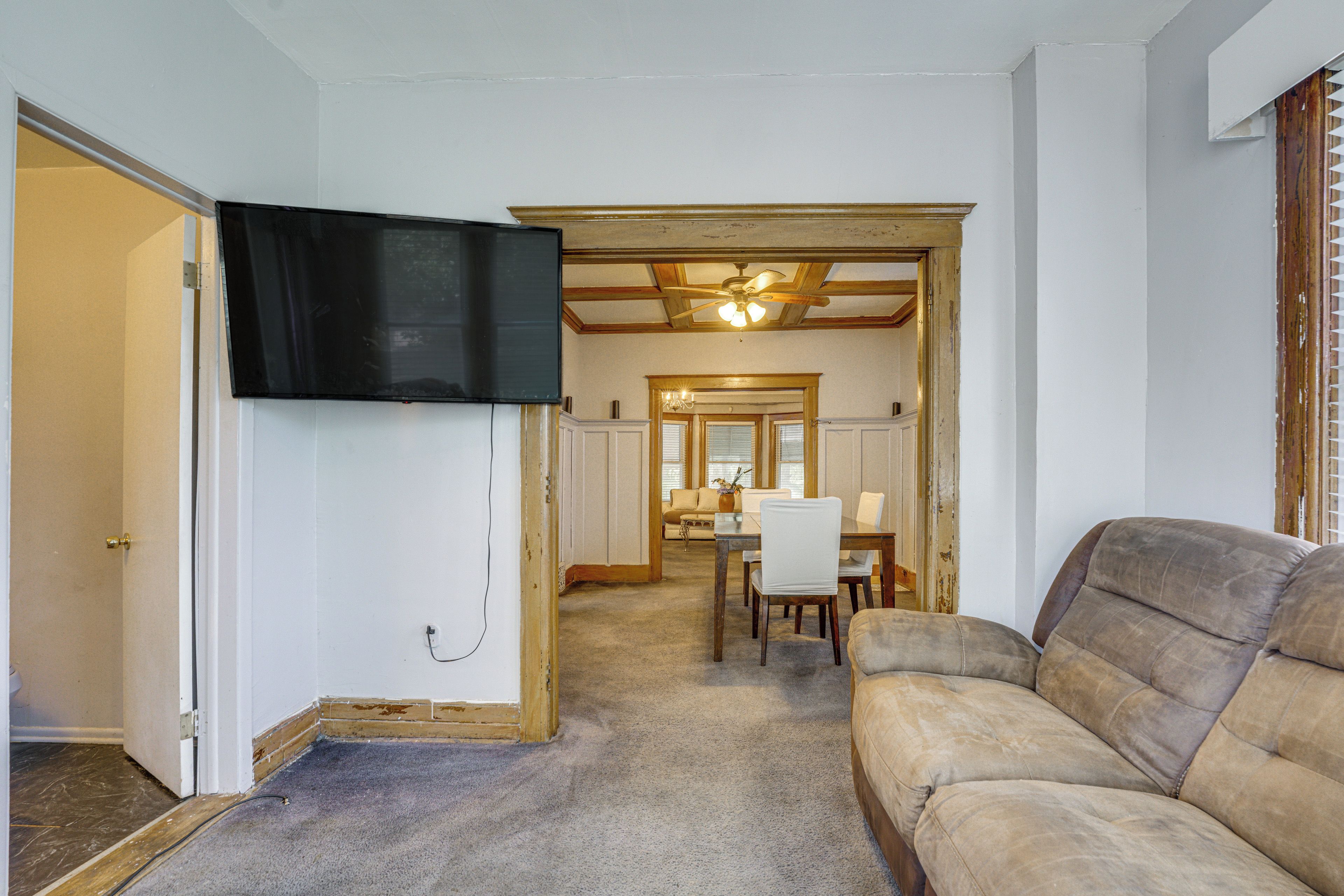 Una sala de estar con un televisor montado en la pared, un sofá marrón y un comedor con mesa y sillas.