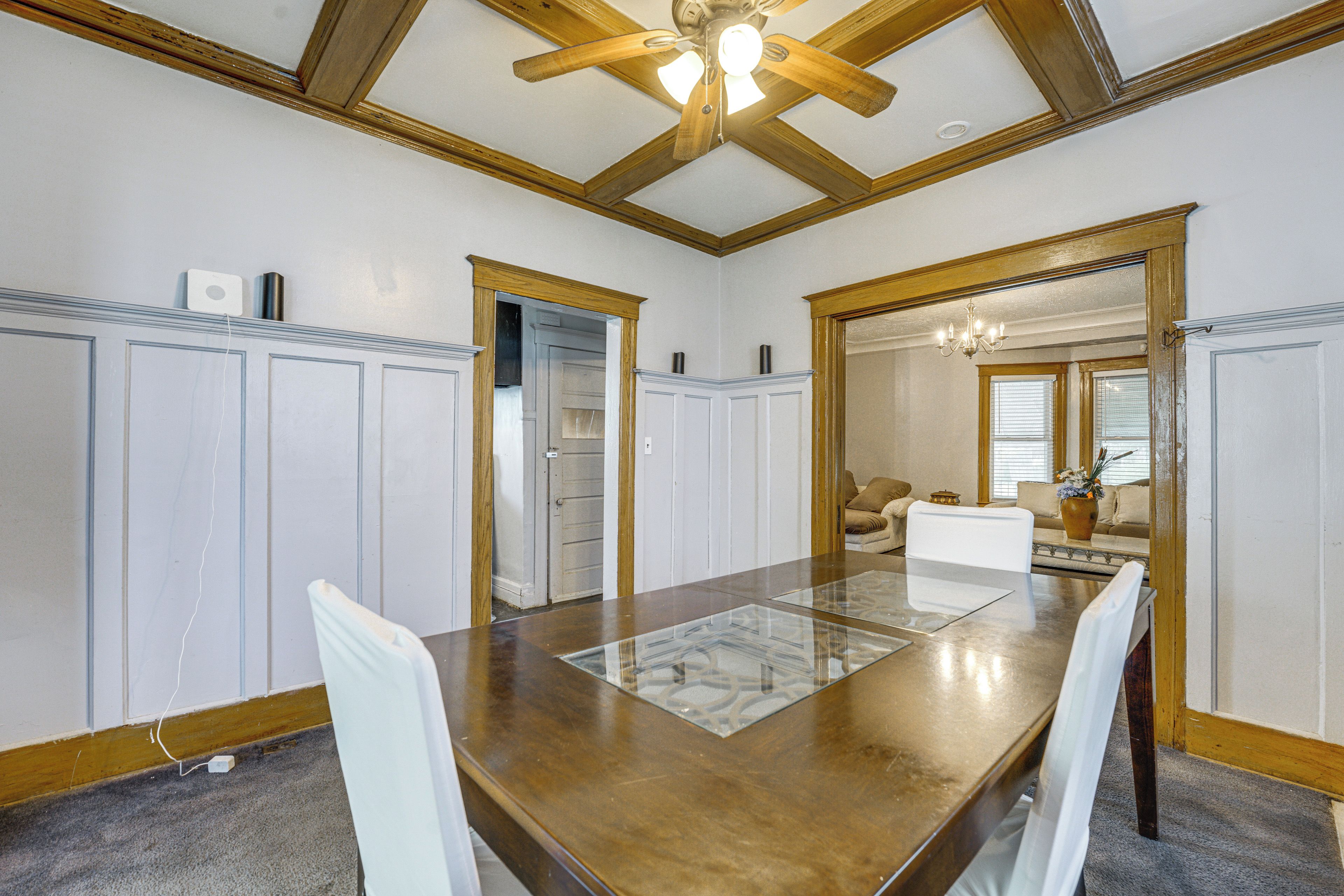 A dining room with a wooden table and chairs, white walls, and a ceiling fan.