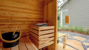 Sala de sauna com paredes de madeira, um recipiente preto e um banco de madeira.