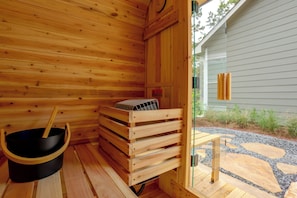 Una sala de sauna con paredes de madera, un recipiente negro y un banco de madera.