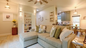 Sala de estar com sofá seccional, área de jantar com mesa e cadeiras, cozinha ao fundo e ventilador de teto.