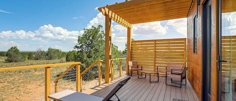 A wooden deck with outdoor furniture, a pergola, and a view of the surrounding landscape.
