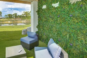 A patio area with a seating arrangement, a wall covered in greenery, and a view of a body of water. - Outdoor Oasis! Luxe Waterfront Gem in Lehigh Acres (Lehigh Acres)