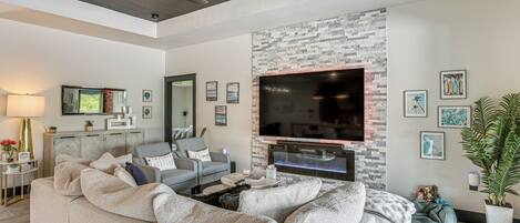 Una sala de estar moderna con un sofá seccional, un televisor de pantalla plana montado en una pared de piedra y una chimenea.