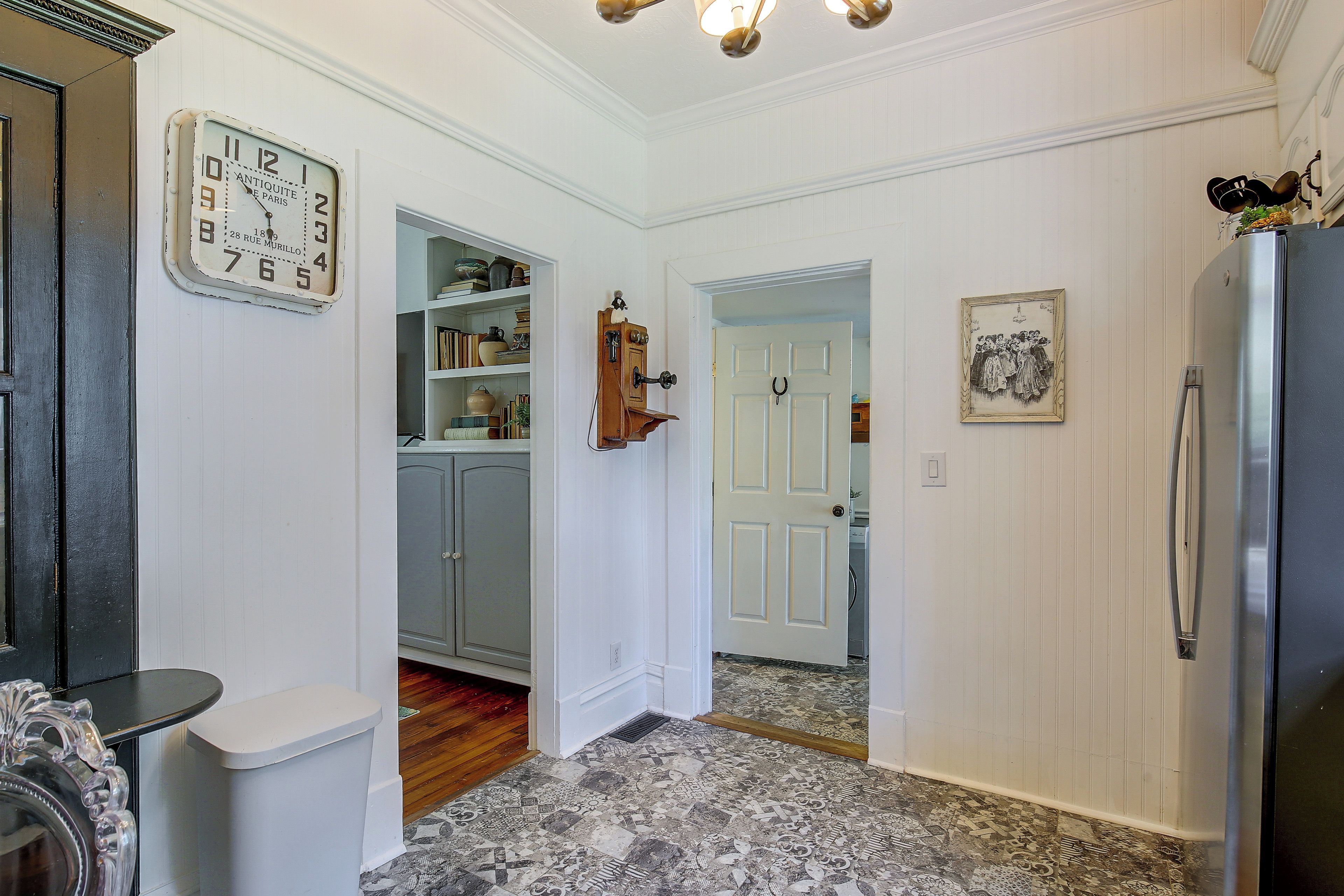 A hallway with a vintage wall clock, a door leading to a laundry area, and a refrigerator.