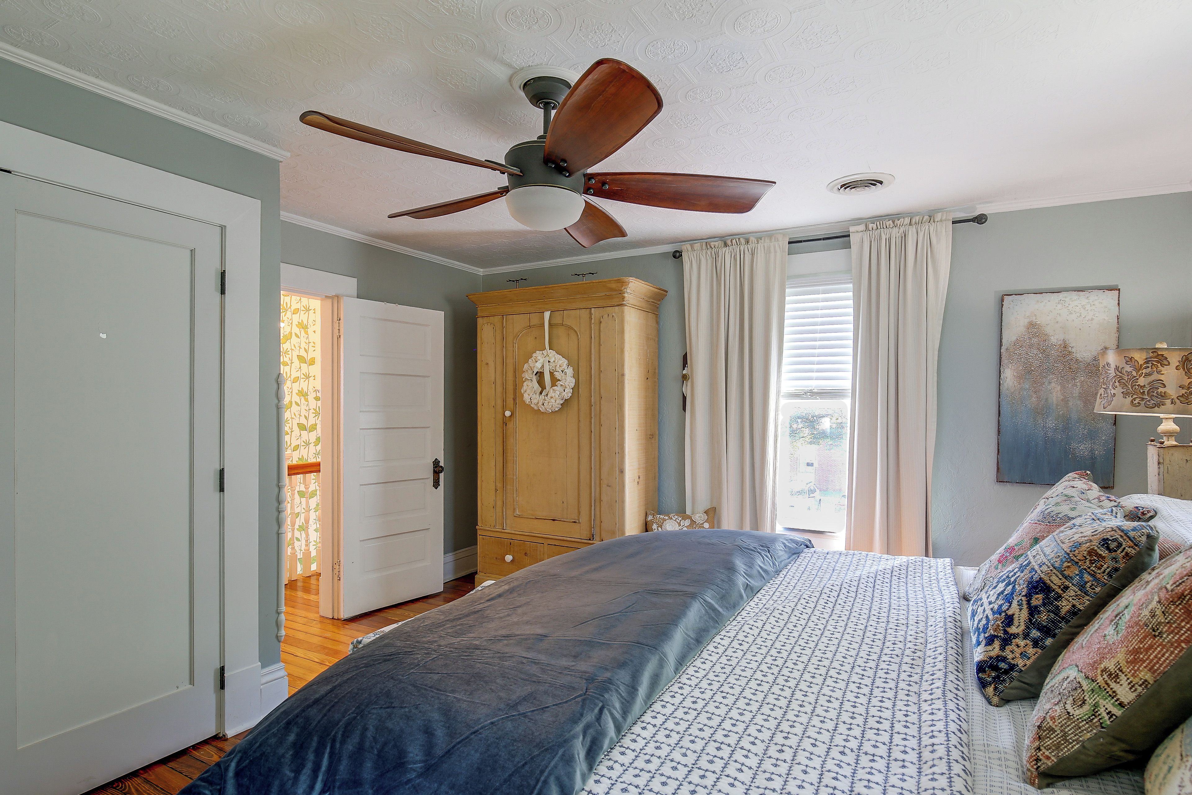 A bedroom with a bed, a ceiling fan, a wardrobe, and a window with curtains.