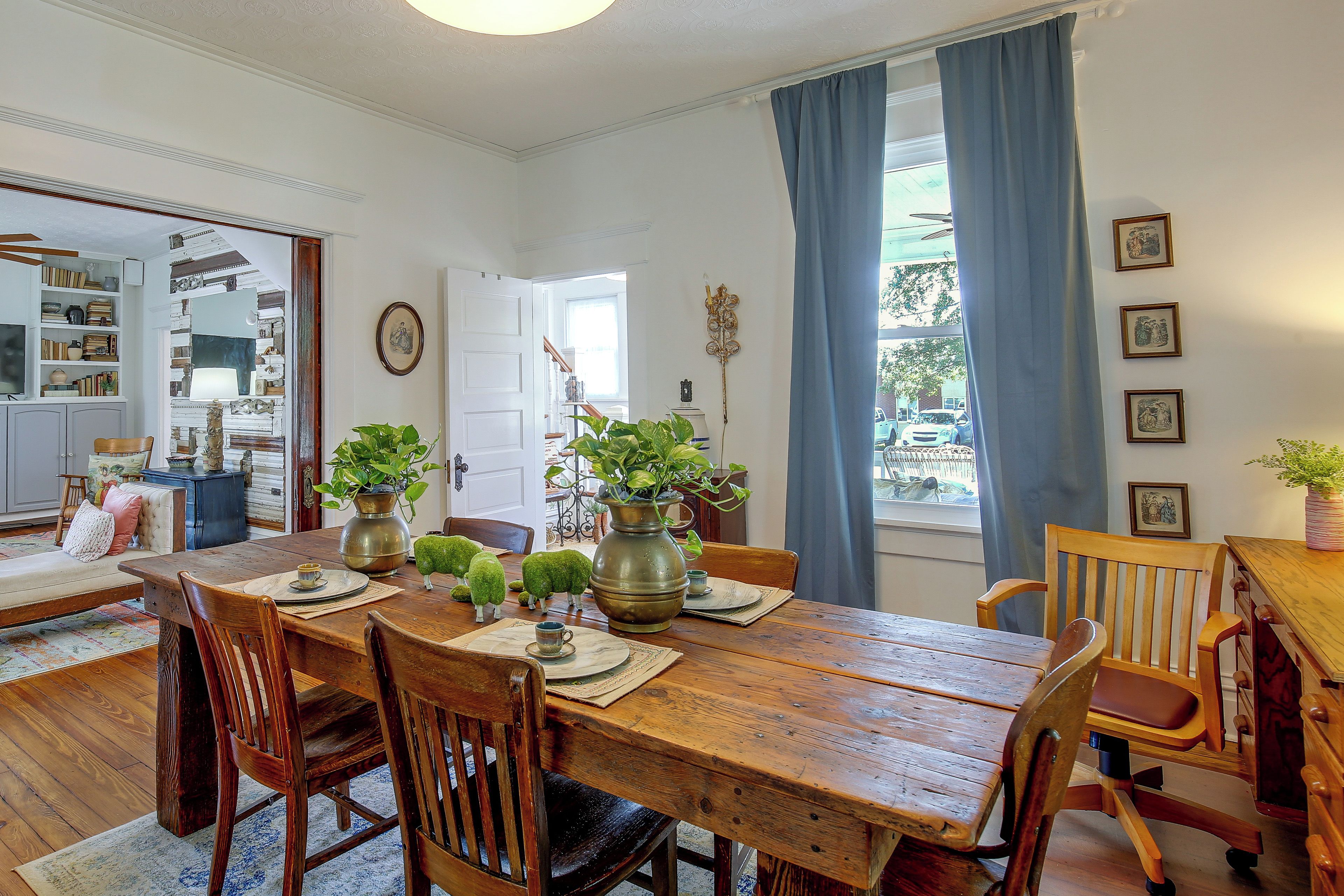 A dining room with a wooden table, chairs, and a view of the outside through a window with blue curtains.