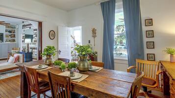 A dining room with a wooden table, chairs, and a view of the outside through a window with blue curtains.