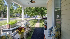 A covered porch with a rocking chair, a table with a potted plant, and a view of a residential street. - Shop, Dine, Explore Dtwn! Walkable Farmington Home (Farmington)
