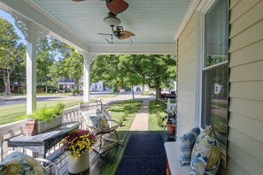 A covered porch with a rocking chair, a table with a potted plant, and a view of a residential street. - Shop, Dine, Explore Dtwn! Walkable Farmington Home (Farmington)